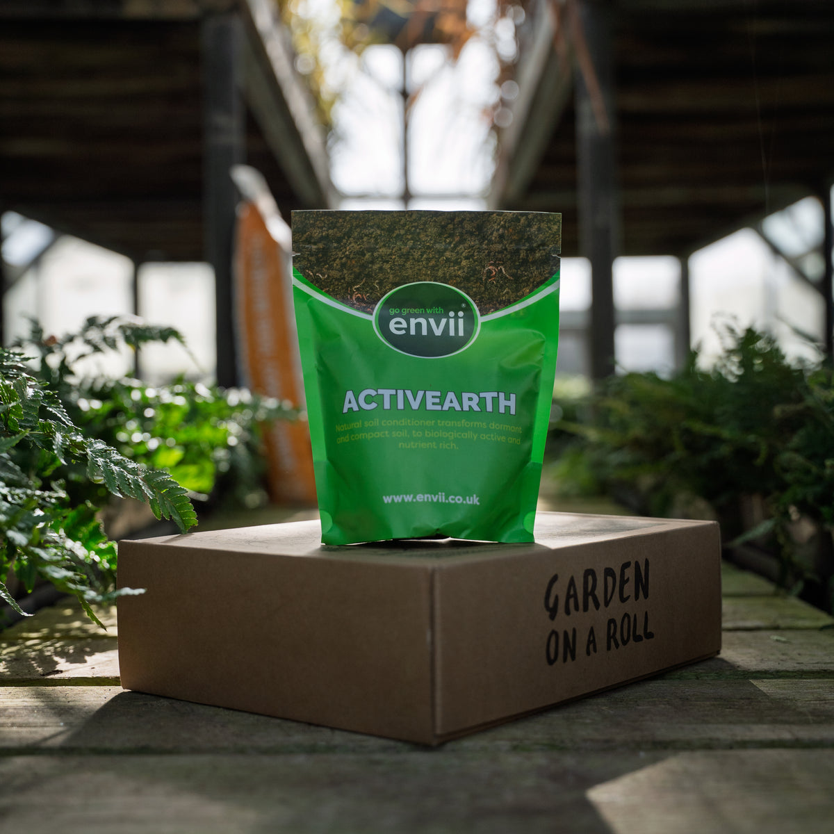 Envii Activearth natural soil conditioner displayed on a Garden on a Roll border box in a greenhouse.
